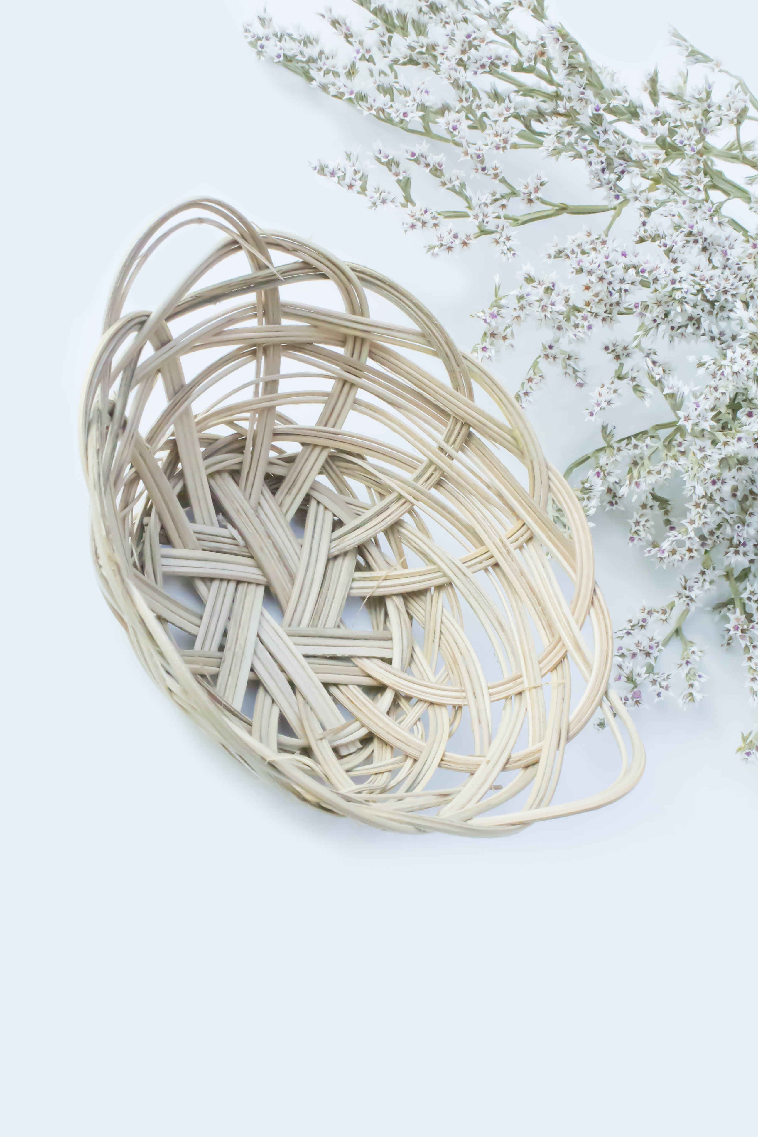 A woven banana leaf basket from Moony Paw, placed on a bed of dried blue and yellow flowers.