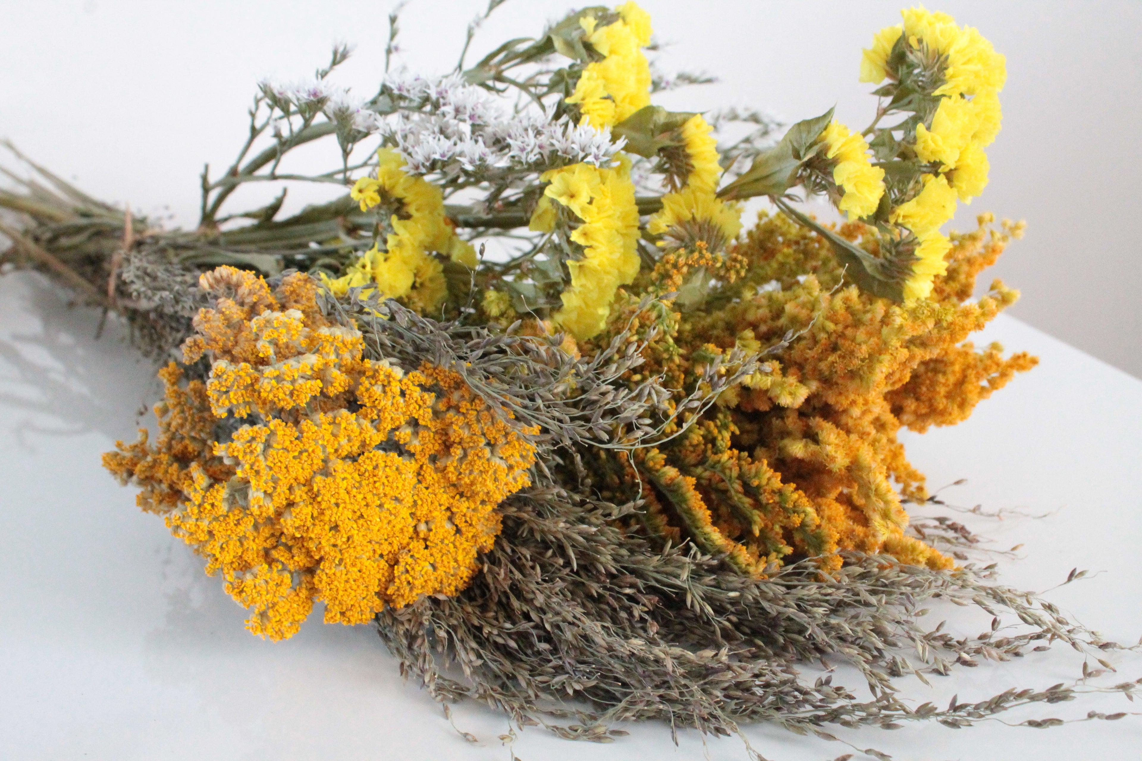 Bouquet of dried yellow and orange flowers on a white surface