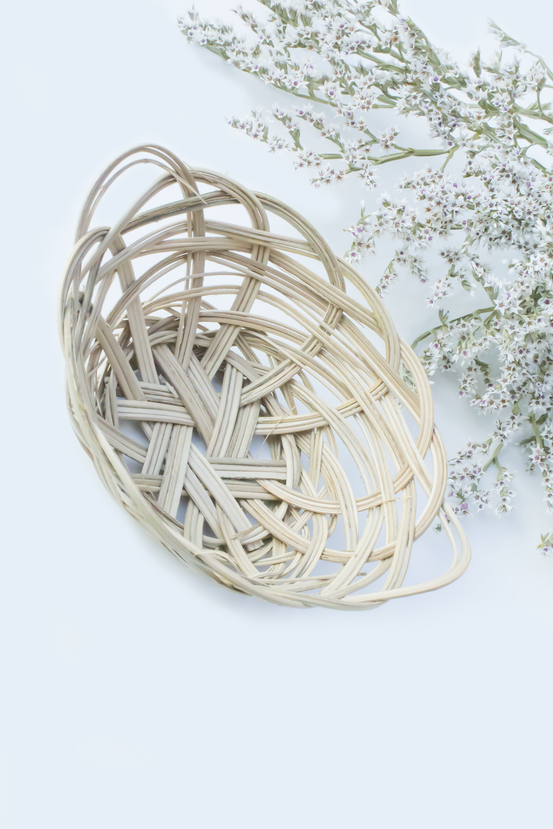 A woven banana leaf basket from Moony Paw, placed on a bed of dried blue and yellow flowers.