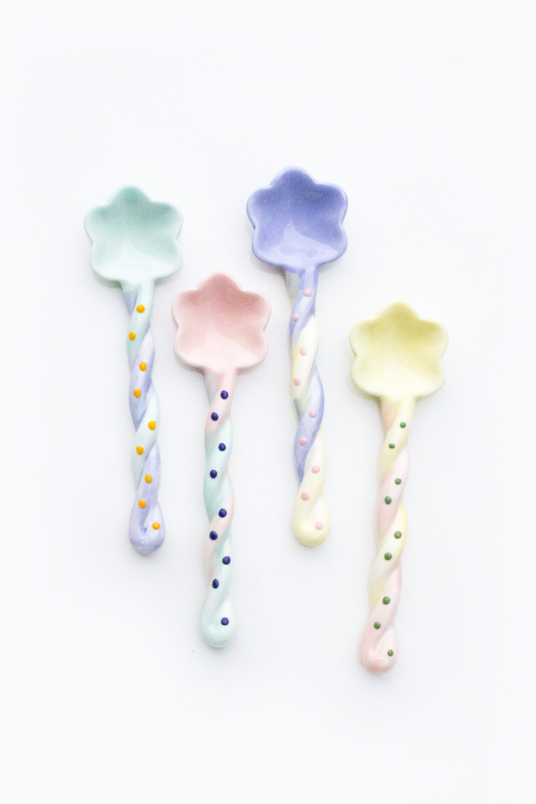 Set of four pastel-colored spoons with floral designs on a white background