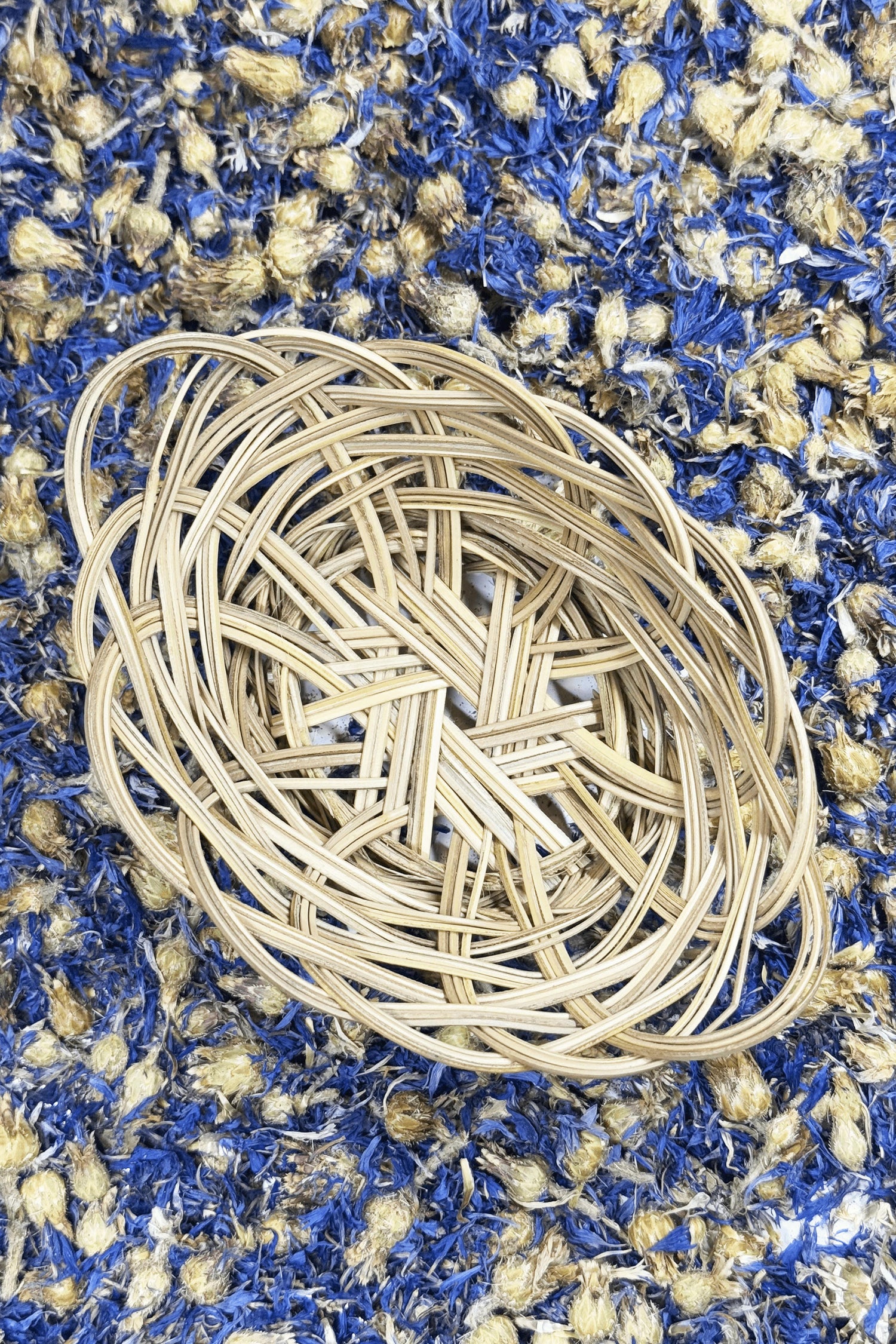 A woven banana leaf basket from Moony Paw, placed on a bed of dried blue and yellow flowers.