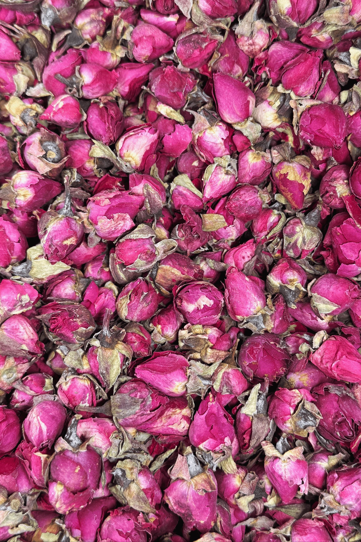 A close-up of dried rose buds in shades of deep pink with hints of green, creating a textured floral display.