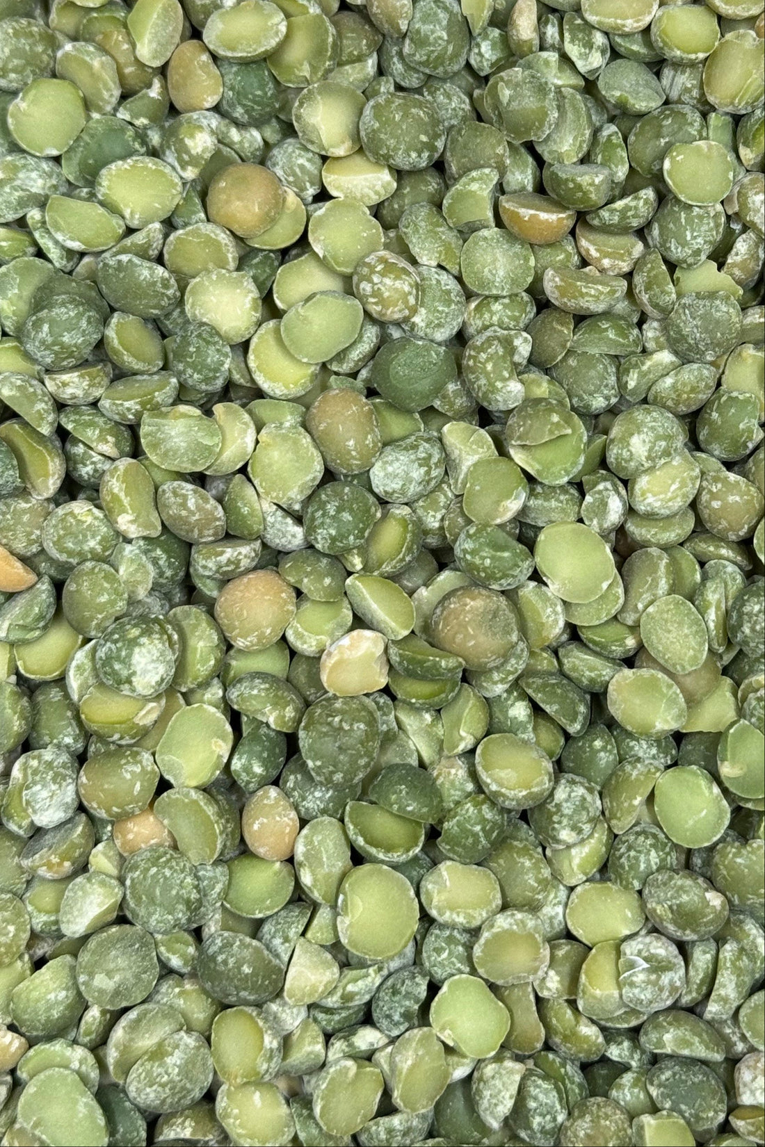 A close-up of dried green split peas with a smooth, slightly powdery texture, filling the entire frame.