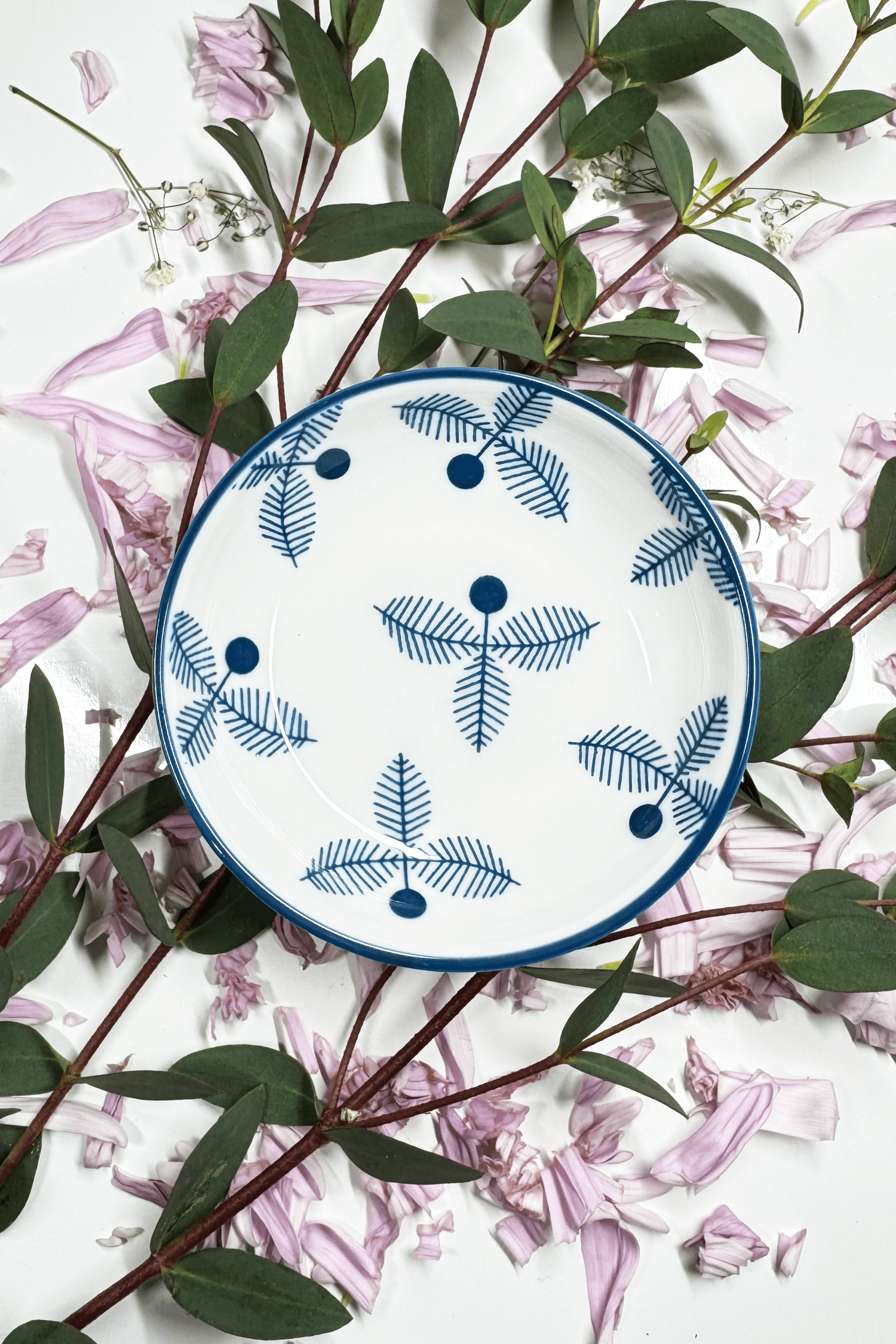 A Sapphire Splash Plate for small animals, featuring a blue fern-like pattern, placed on petals and leaves.