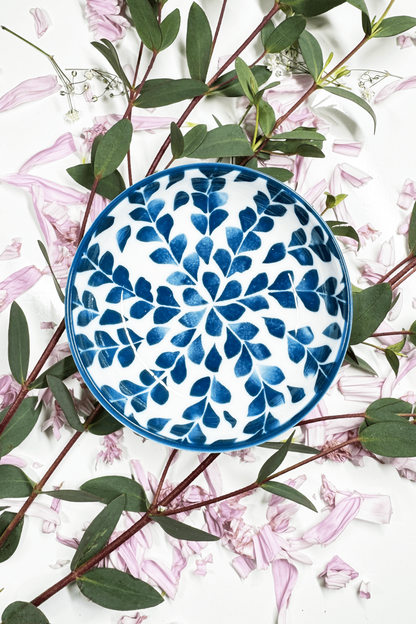 A Sapphire Splash Plate for small animals, featuring a blue leaf pattern, placed on petals and greenery.