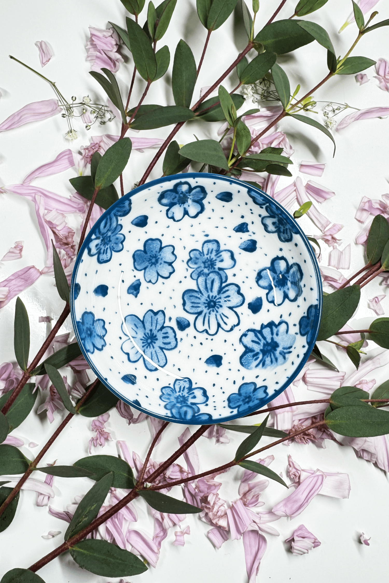 A Sapphire Splash Plate for small animals, featuring a blue floral pattern, placed on petals and greenery.