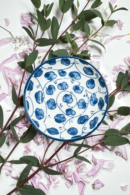 A Sapphire Splash Plate for small animals, decorated with a blue floral design, placed on petals and leaves.