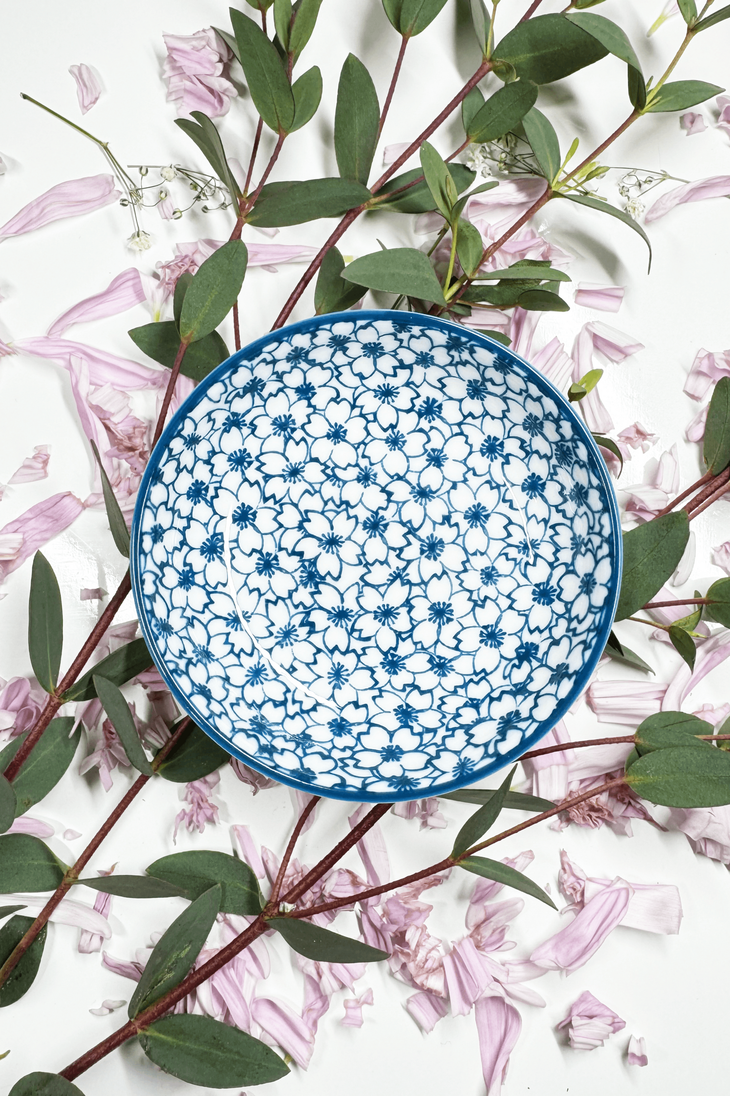 A Sapphire Splash Plate for small animals, featuring a blue floral pattern, placed on petals and greenery.